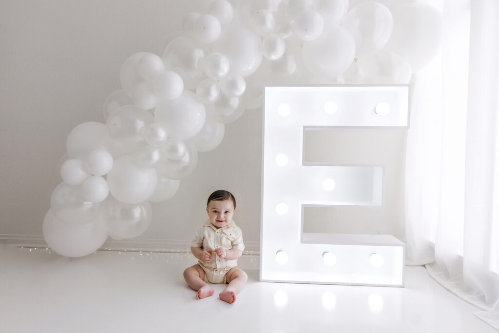 baby sitting with balloon garland and marquee letter